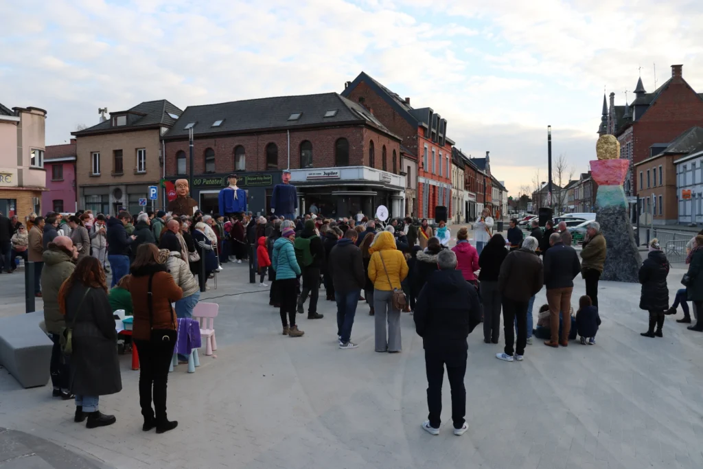 Rassemblement de personnes sur une place publique bordée de bâtiments, lors d’un événement en plein air.