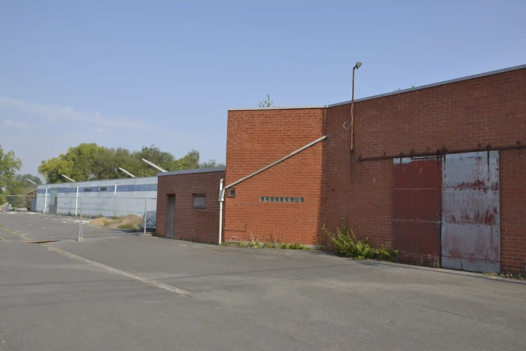 Bâtiment industriel en briques avec porte métallique dans une zone d’activité.