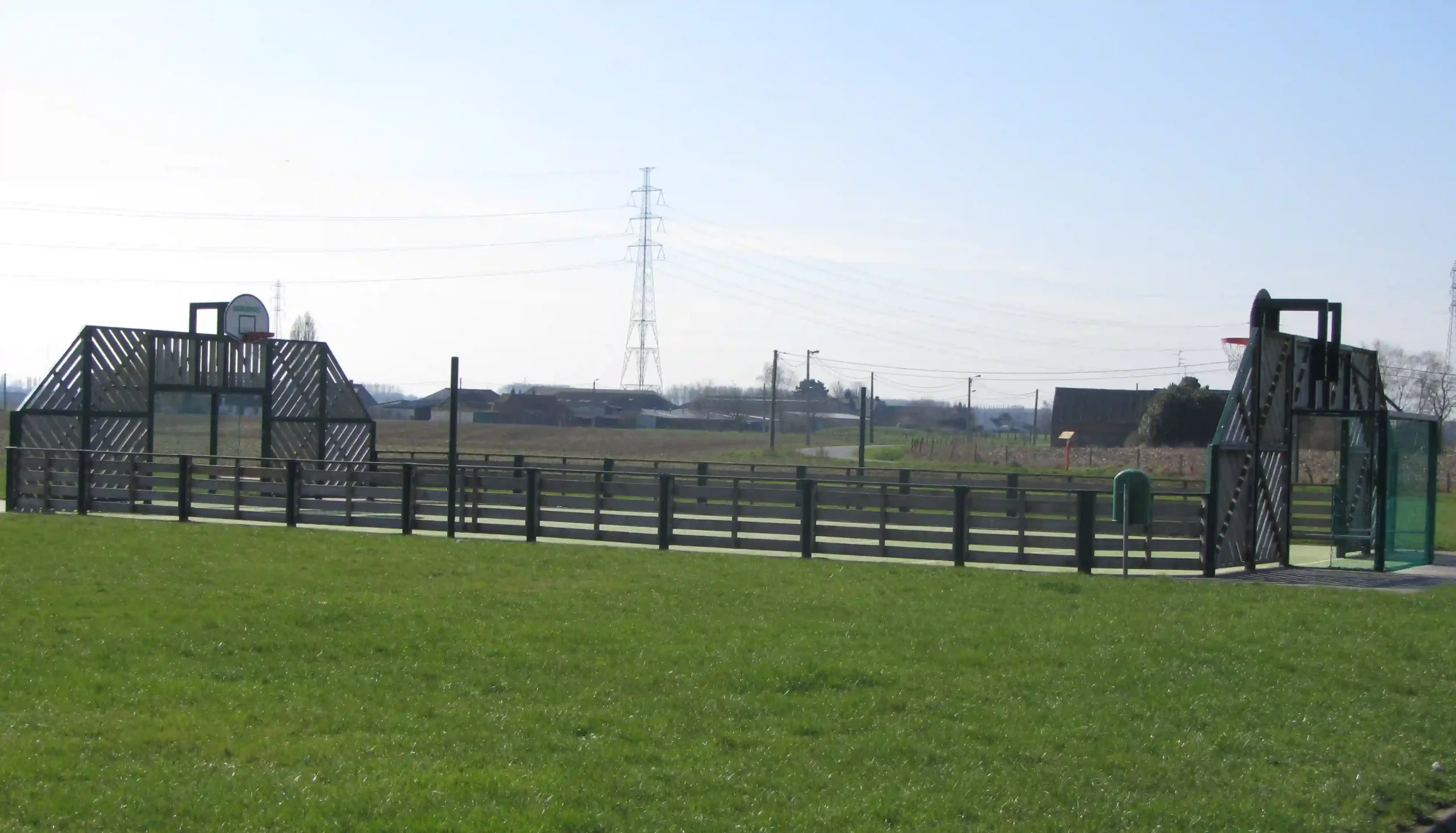 Terrain de sport extérieur avec structures de jeu et terrain de basket en zone rurale.