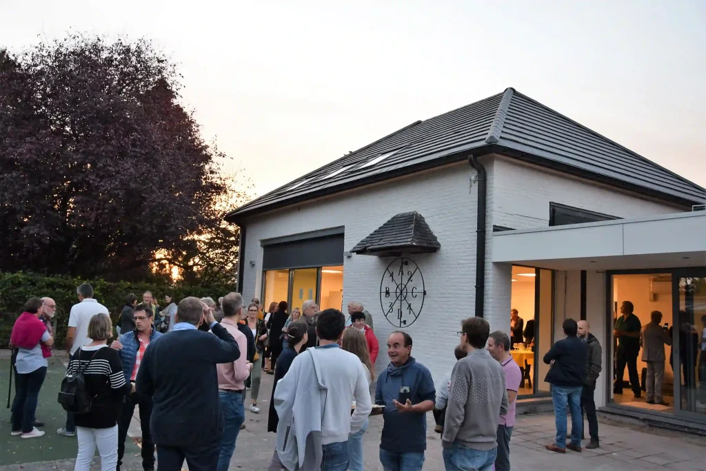 Groupe de personnes rassemblées devant un bâtiment moderne lors d’un événement convivial extérieur.