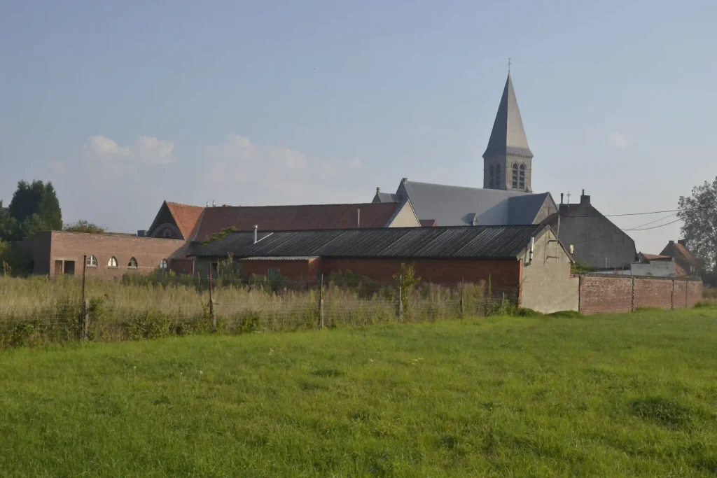 Bâtiments ruraux et clocher d’église vu depuis un champ verdoyant.