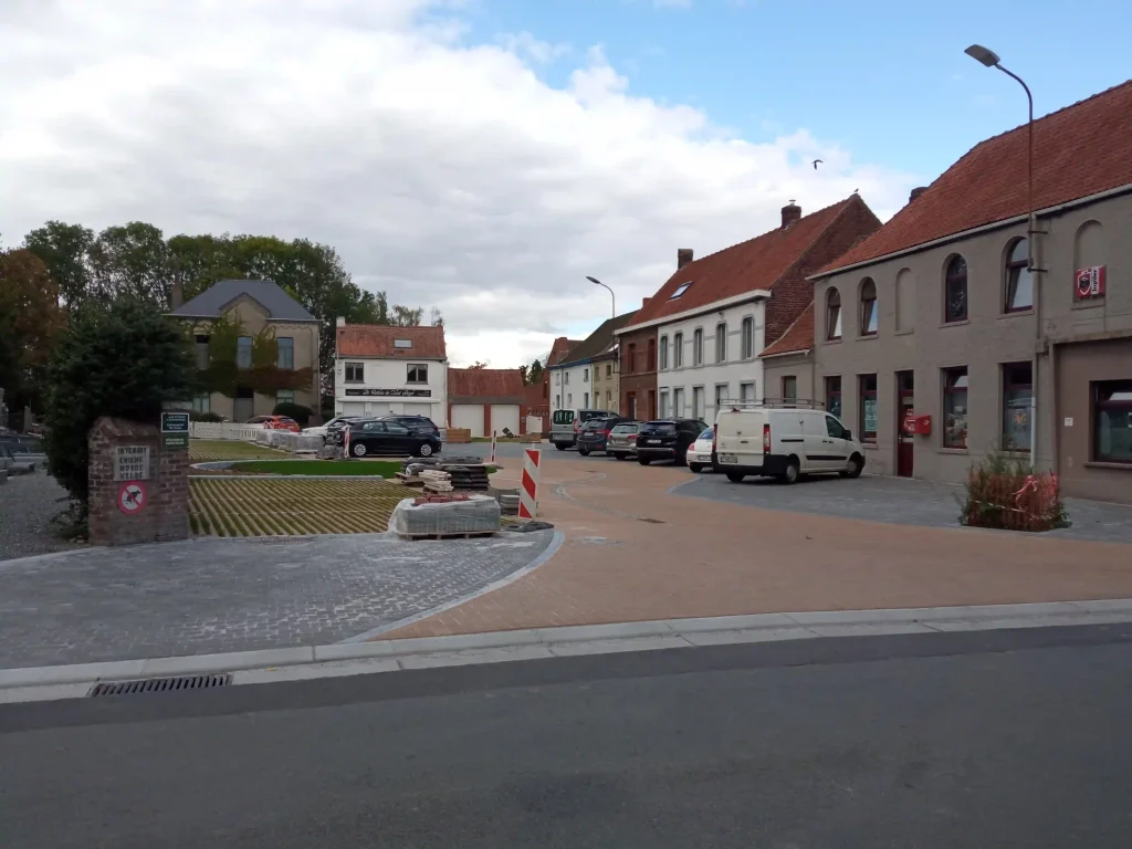 Place de village avec bâtiments en briques, stationnement et voirie aménagée.