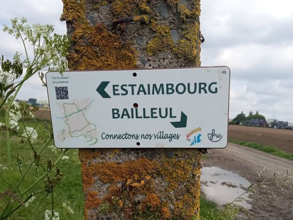Panneau directionnel « Estaimbourg / Bailleul » fixé sur un poteau en milieu rural.