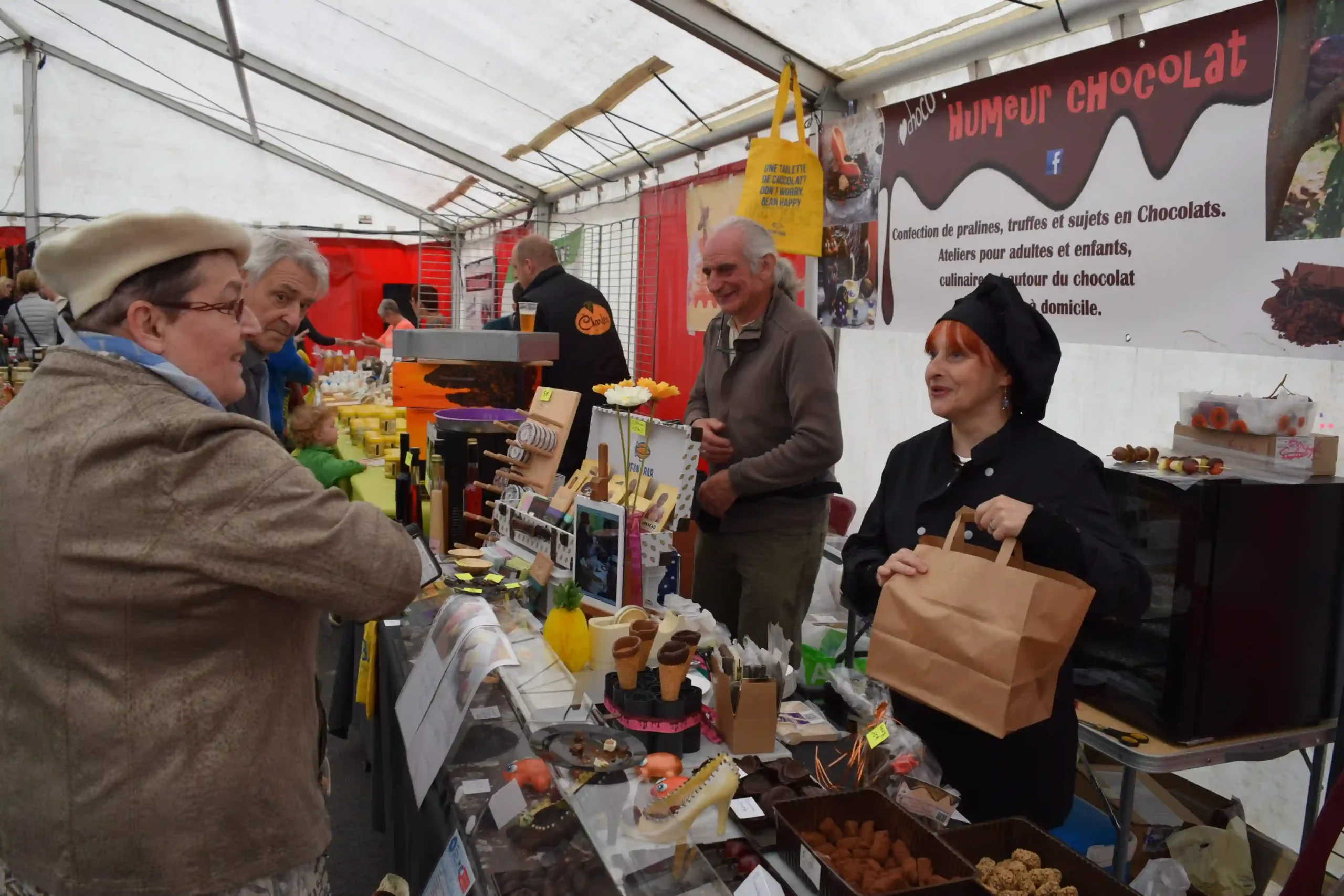 Stand de marché avec produits artisanaux et échanges entre visiteurs et exposants.