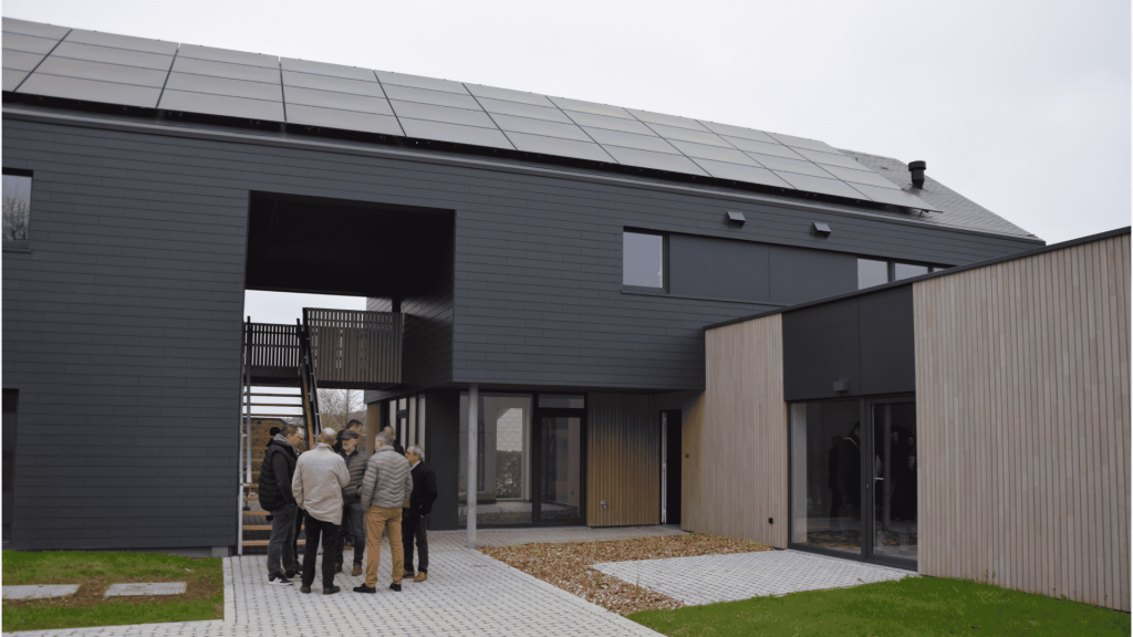 Logements intergénérationnels à Manhay : bâtiments modernes aux grandes fenêtres & aperçu des aménagements extérieurs.