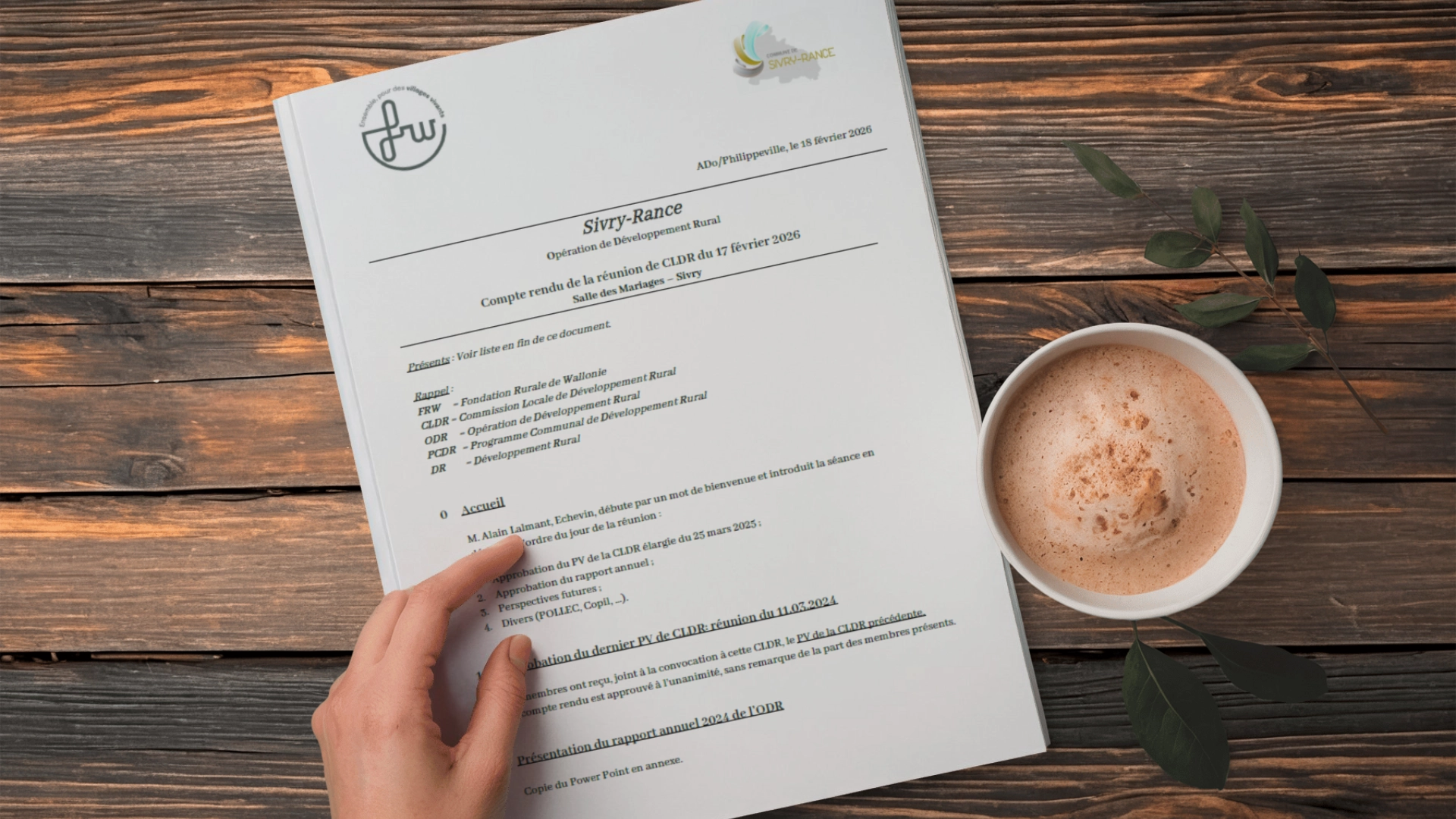 Main tenant un document administratif posé sur une table en bois, à côté d’une tasse de café.