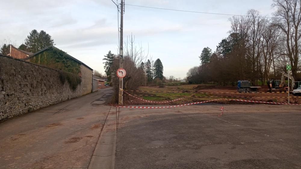 Vue du centre du village de Sautin avant réaménagement. L’image montre un carrefour bordé de maisons en briques et d’arbres dénudés en hiver. Au premier plan, un panneau de signalisation indique les directions vers Éppe-Sauvage, Rance et Montbliart. Le soleil se couche à l’horizon, créant une lumière douce sur la scène. Cet espace, actuellement marqué par des zones de gravier et des murets en briques, sera prochainement repensé pour offrir un cadre plus convivial et sécurisé aux habitants.